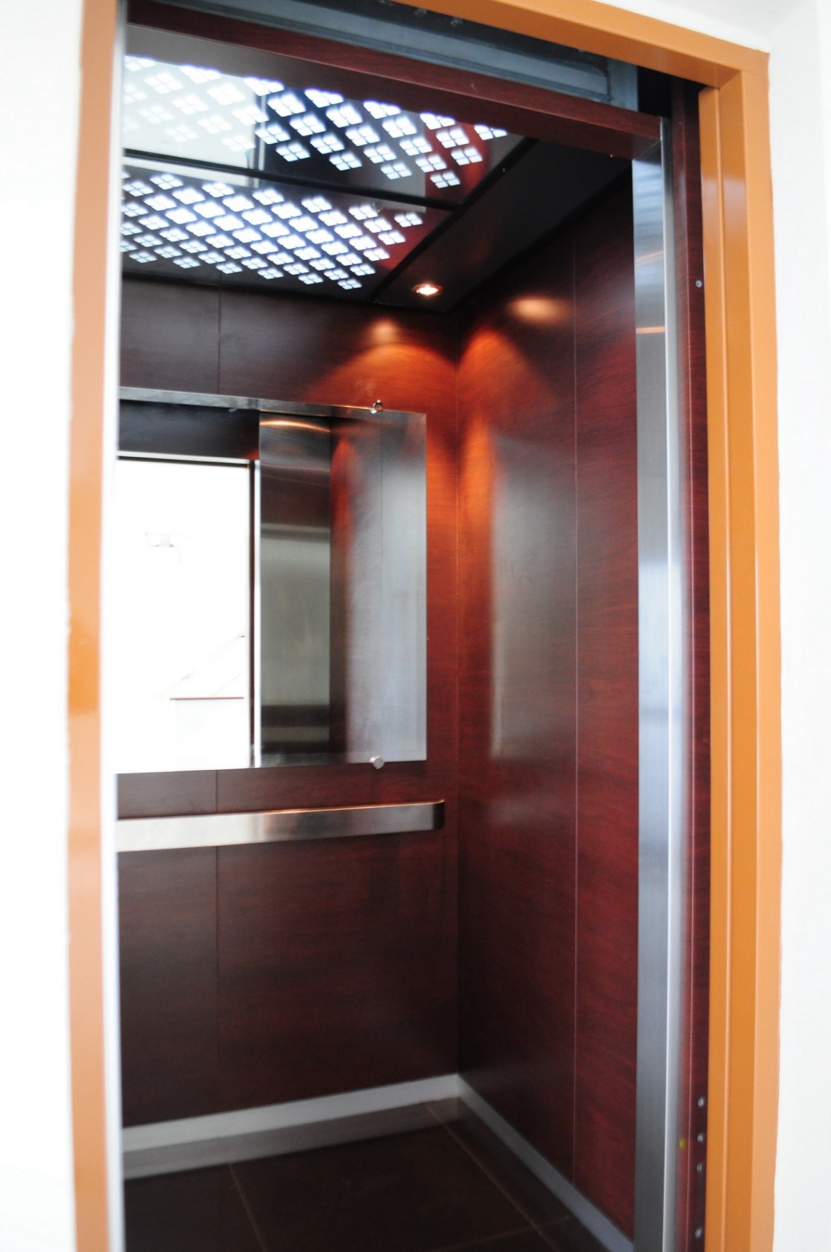 Passenger lift interior with wood-tone walls, a mirror, and handrail